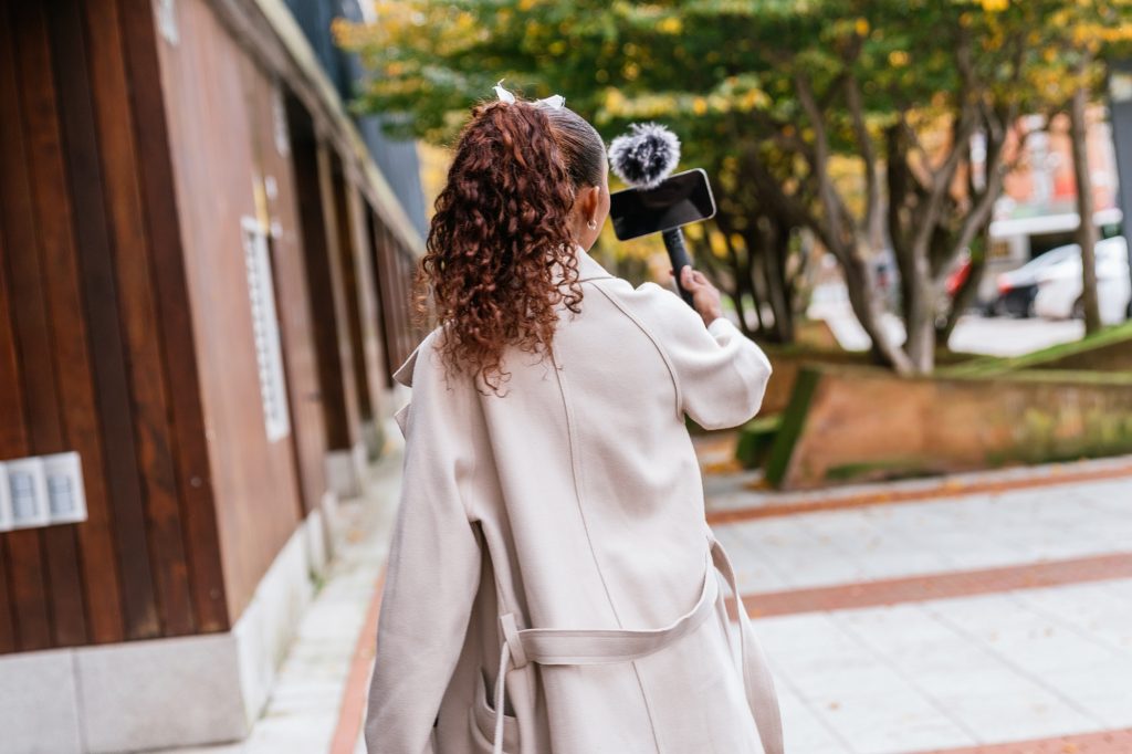 Latin content creator recording outdoor city footage with smartphone and microphone